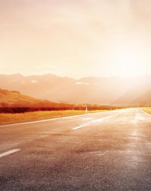 Image looking down an empty road with the sun setting over mountains in the distance