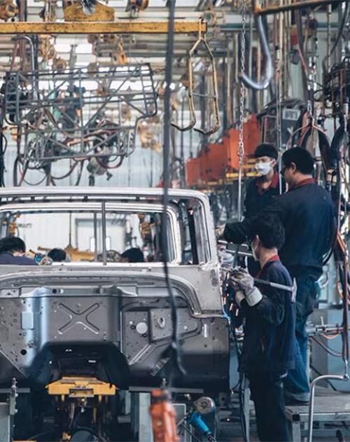 Image of a chinese factory with workers building the steel frame of a car