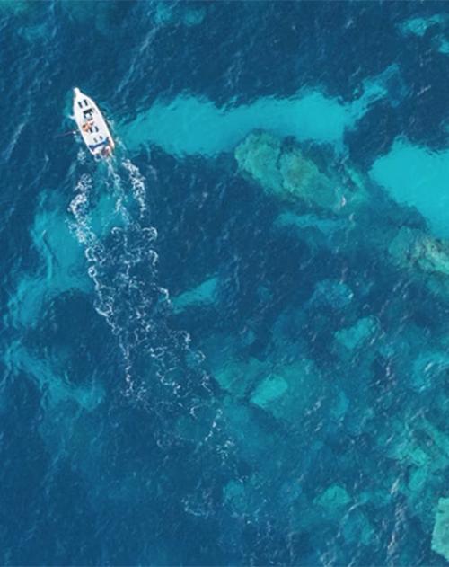 Overhead image of a small white boat in crystal clear blue water 