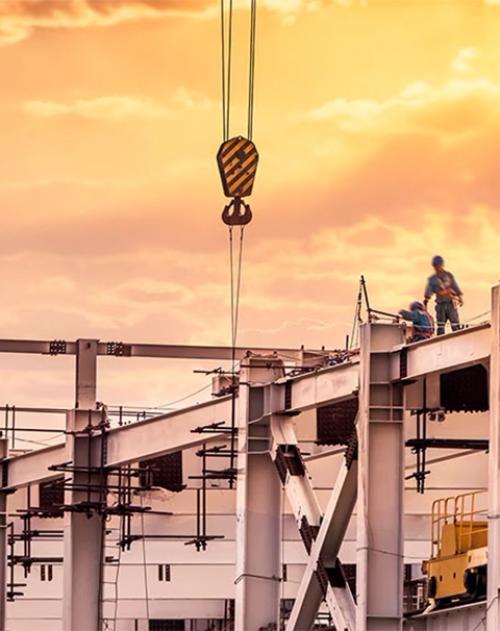 Image of a construction site at sunset with a crane raising steel girders