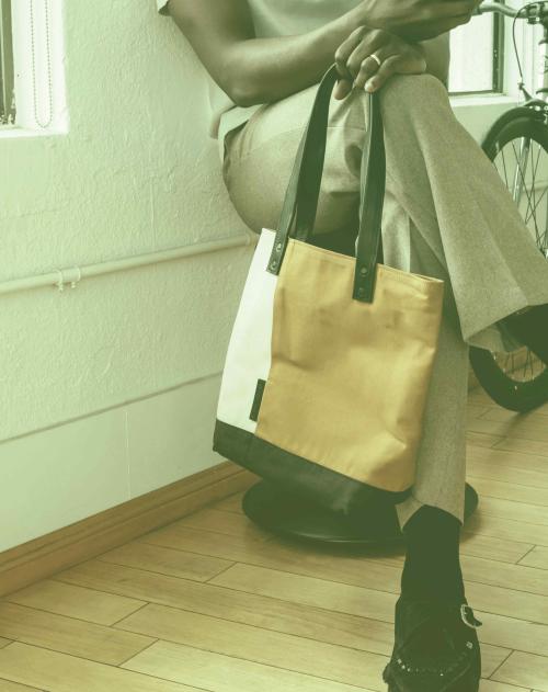 Image of a black man from the chest down sitting holding a phone and bag