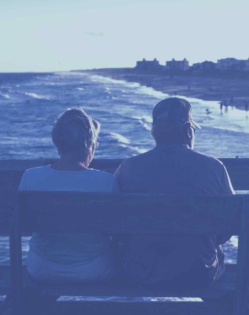 Older couple from behind sitting on a bench looking at a beach and ocean