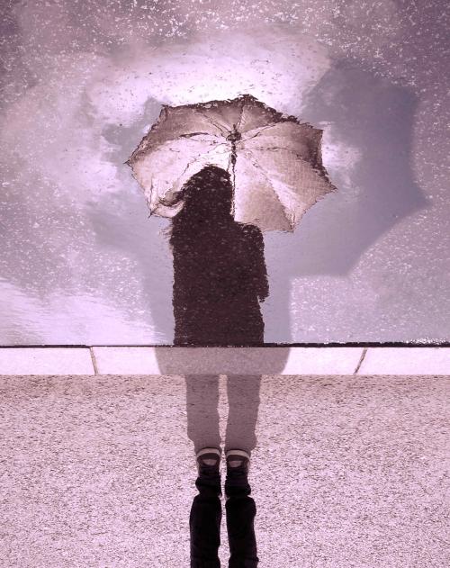 Image of a woman holding an umbrella reflected in a puddle