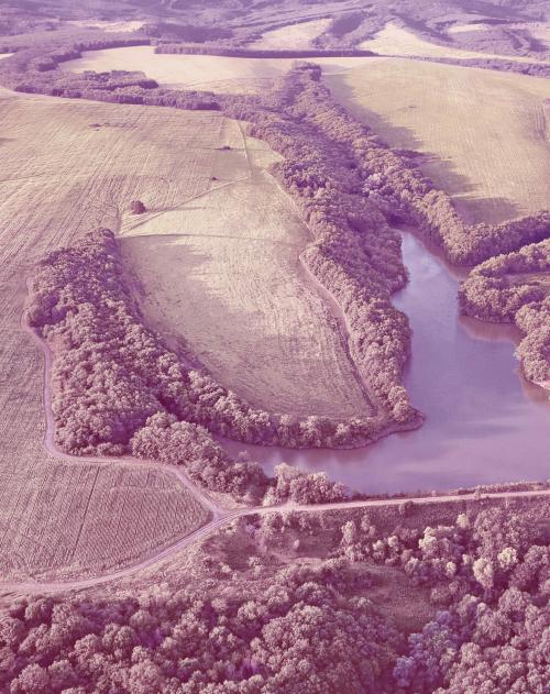 Image of a small lake surrounded by lush green fields and hills taken from above