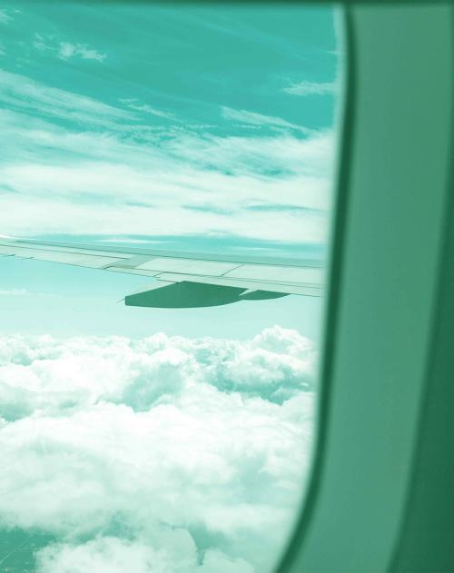 A plane wing can be seen through the airplane window, flying above the clouds