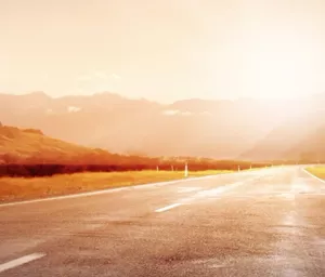 Image looking down an empty road with the sun setting over mountains in the distance